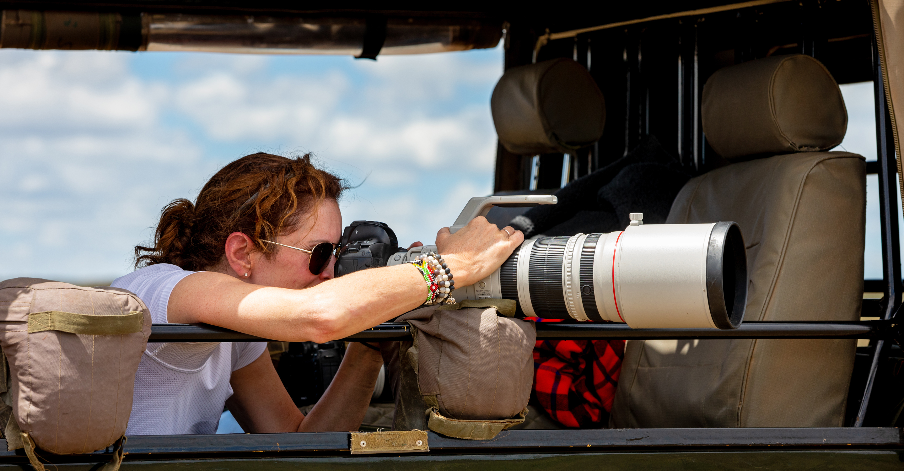 A professional photographer on safari rests her camera on a bean bag and photographs wildlife in the Maasai Mara, Kenya