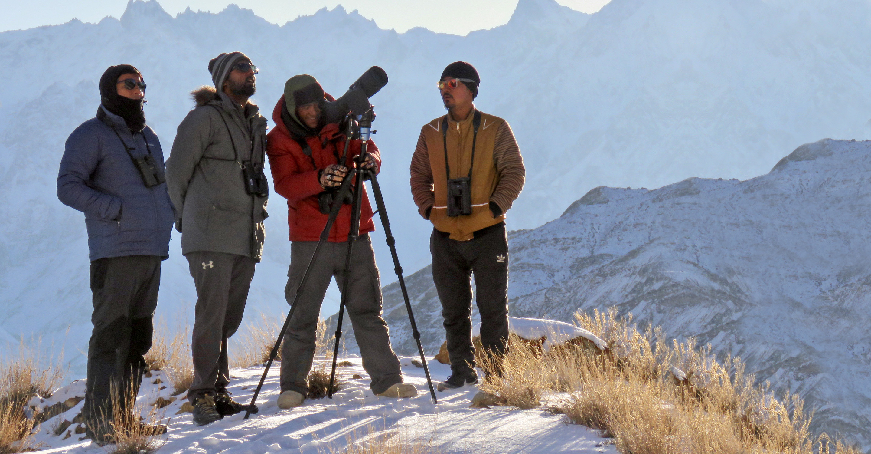 Travelers use a scope to look for snow leopards in a snowy Ladakh, India