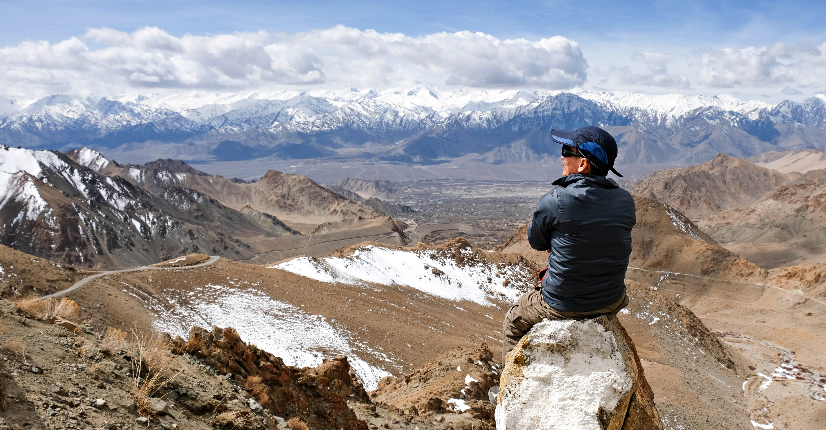 A man sits on a rock overlooking the Himalayan mountain range outside of Ladakh, India