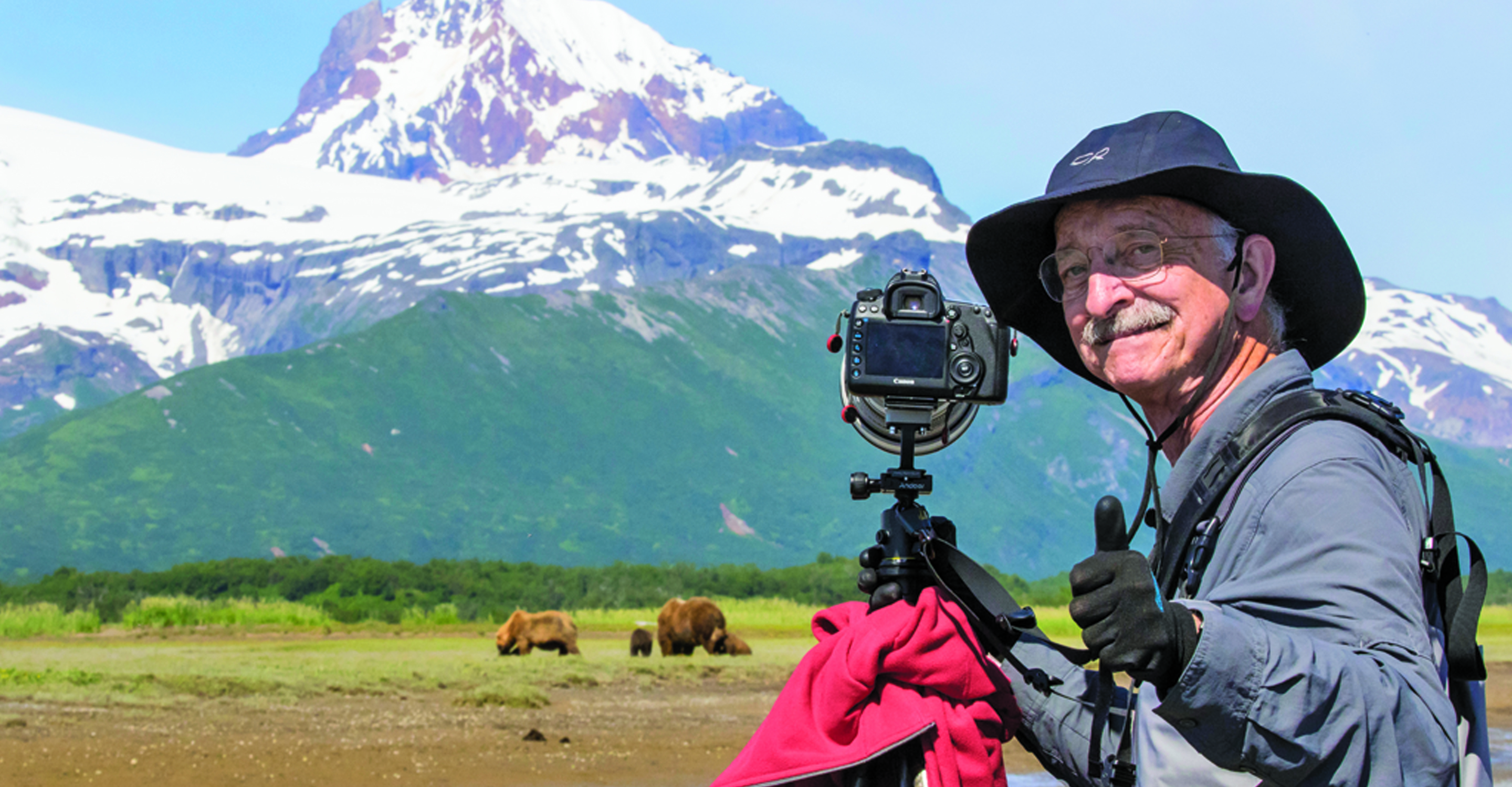 A traveler smiles at the camera after photographing the brown bears in front of him, Katmai National Park, USA