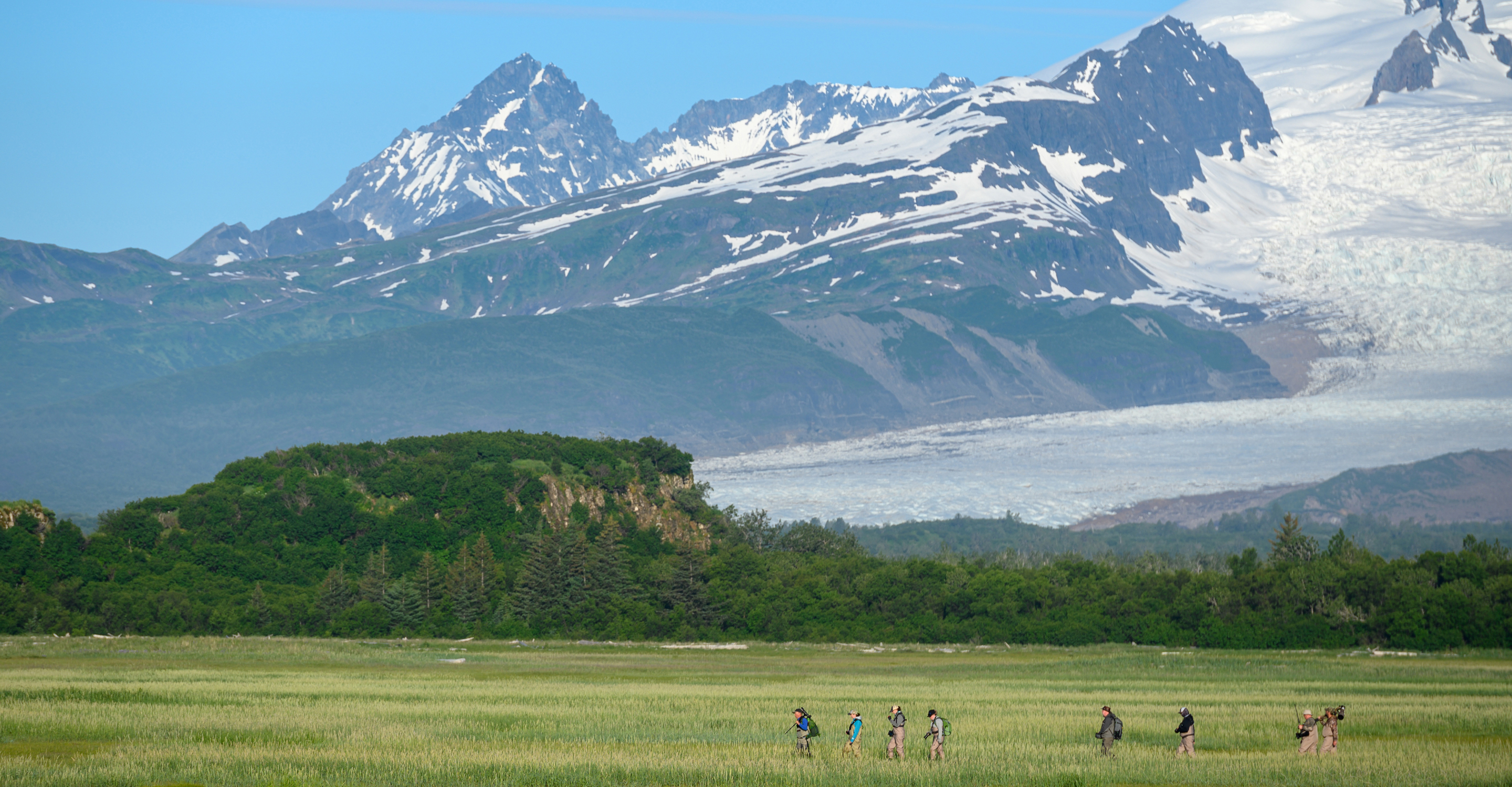 Travelers walk through a valley in front of the Aleutian mountain range in Katmai National Park, Alaska, USA