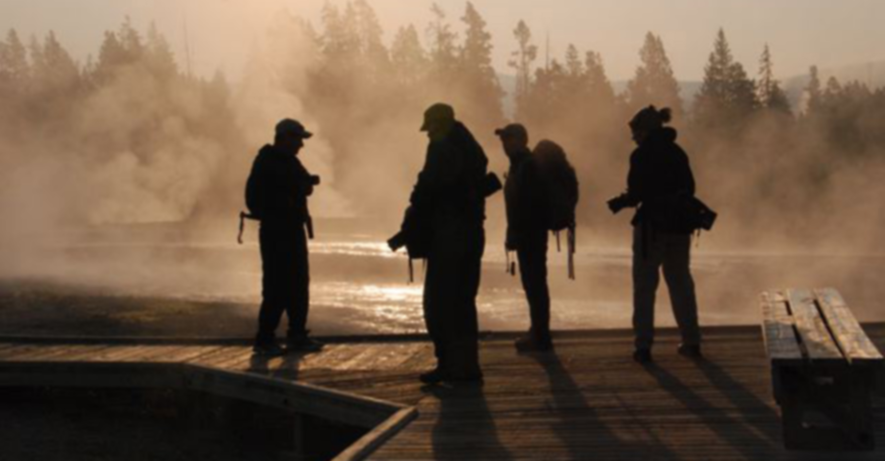 Photographers in a boardwalk are silhouetted against the sunset, Yellowstone National Park, United States