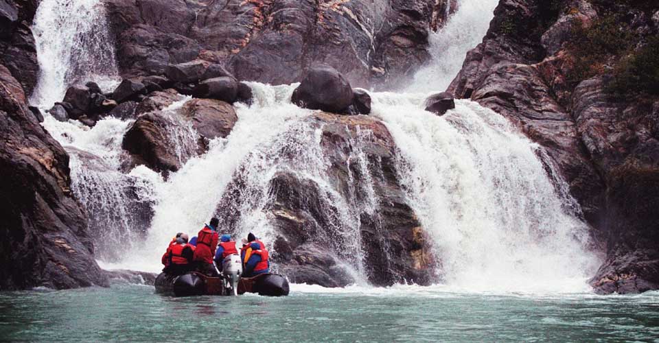 Travelers view a waterfall from a zodiac, Alaska