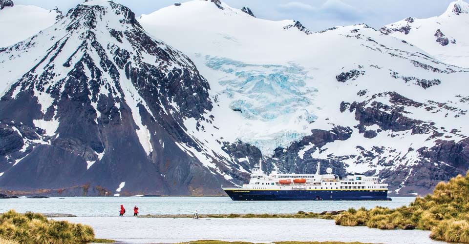Travelers stand ashore near the National Geographic Explorer as it anchors near a glacier, South Georgia, Antarctica