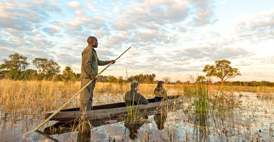 Two travelers sit in a mokoro paddled by a guide in the Okavango Delta, Botswana