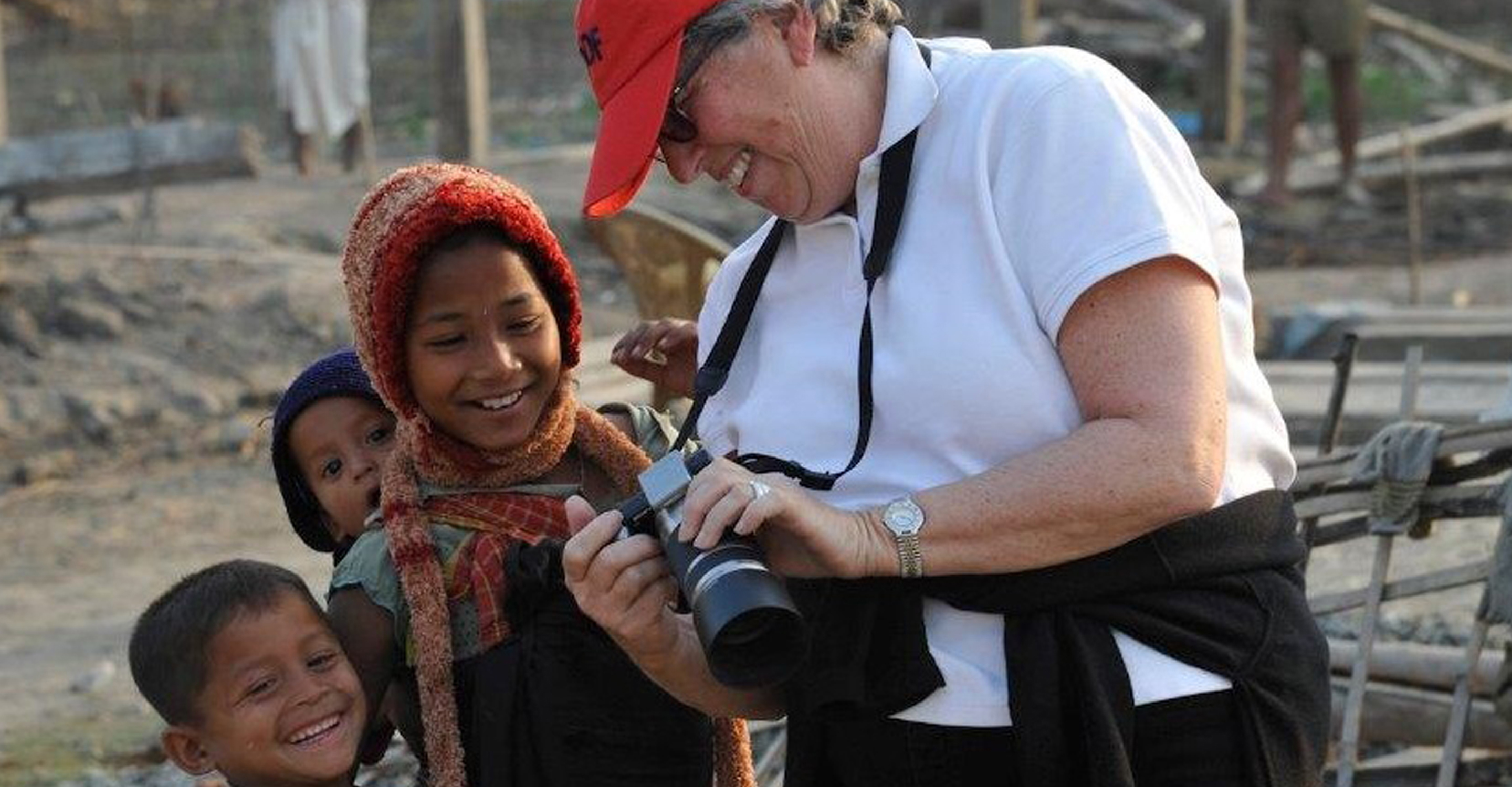 A traveler shows local children a photo she took on her camera while visiting India