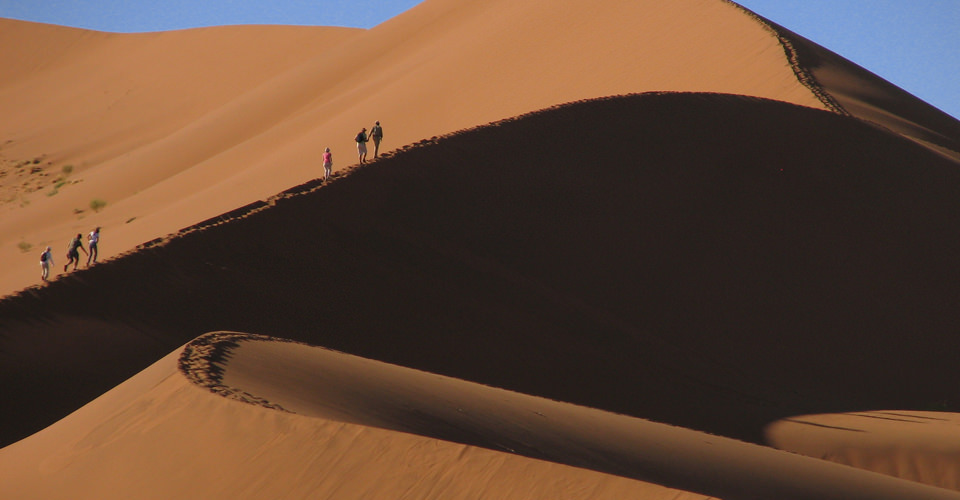Travelers hike the ridgeline of a red sand dune in Sossusvlei, Namib-Naukluft National Park, Namibia