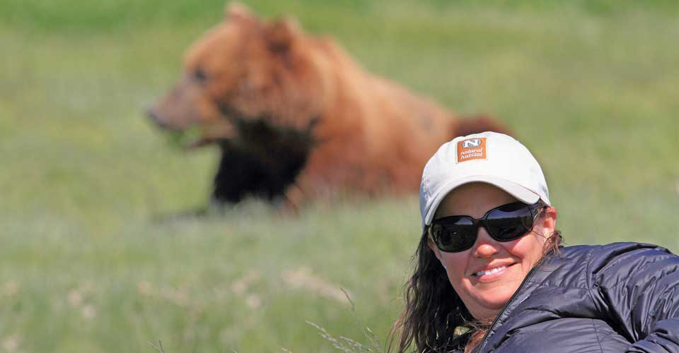 A traveler smiles in front of a brown bear in Katmai National Park, Alaska, USA
