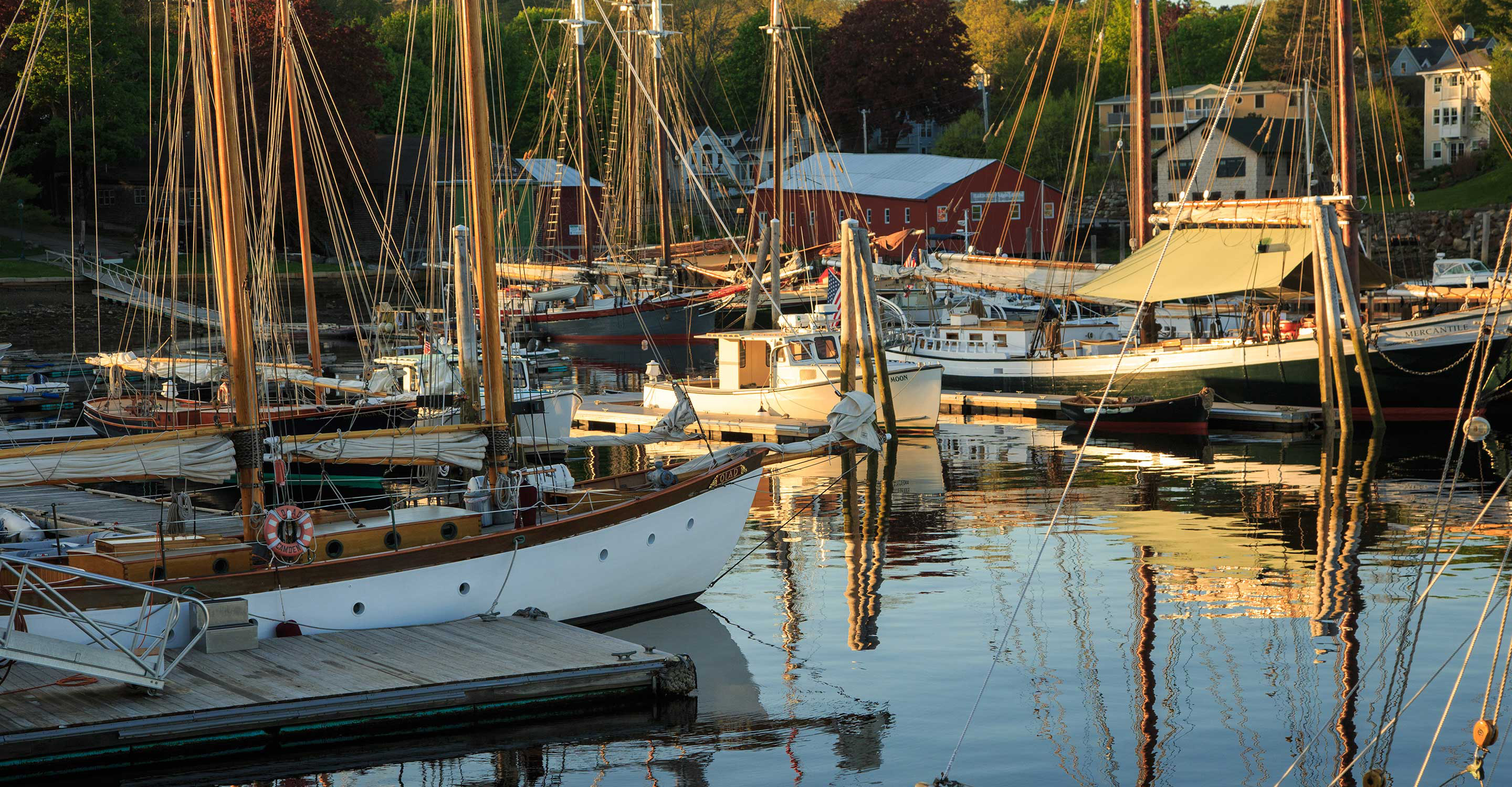 Boats sit in Camden, Maine harbor with bright fall foliage in Autumn