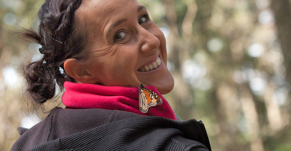 A traveler smiles with a monarch butterfly on her shoulder, Chincua Butterfly Sanctuary, Mexico