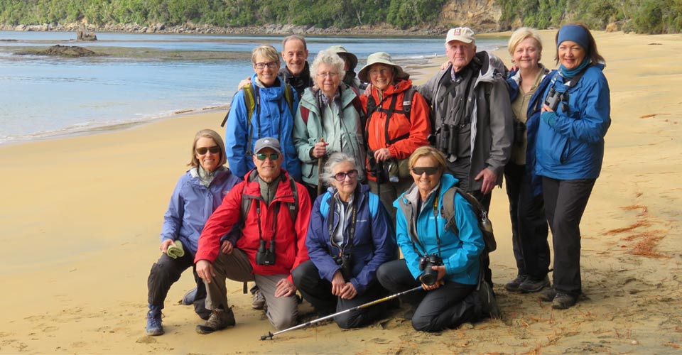 A group of Natural Habitat Adventures travelers pose on the beach on Ulva Island, New Zealand