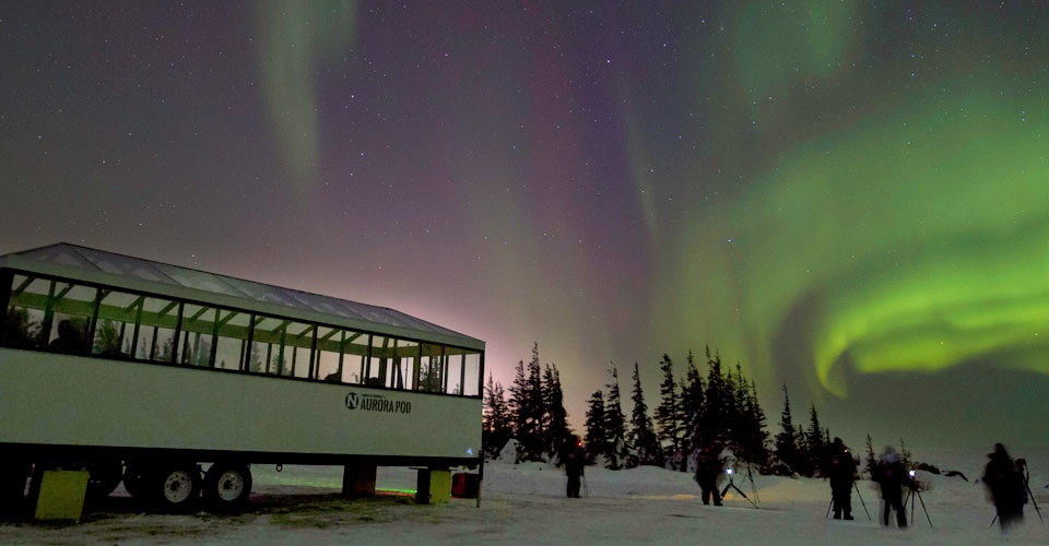 Travelers stand in front of Natural Habitat Adventures' Aurora Pod photographing the northern lights in Churchill, Manitoba, Canada;