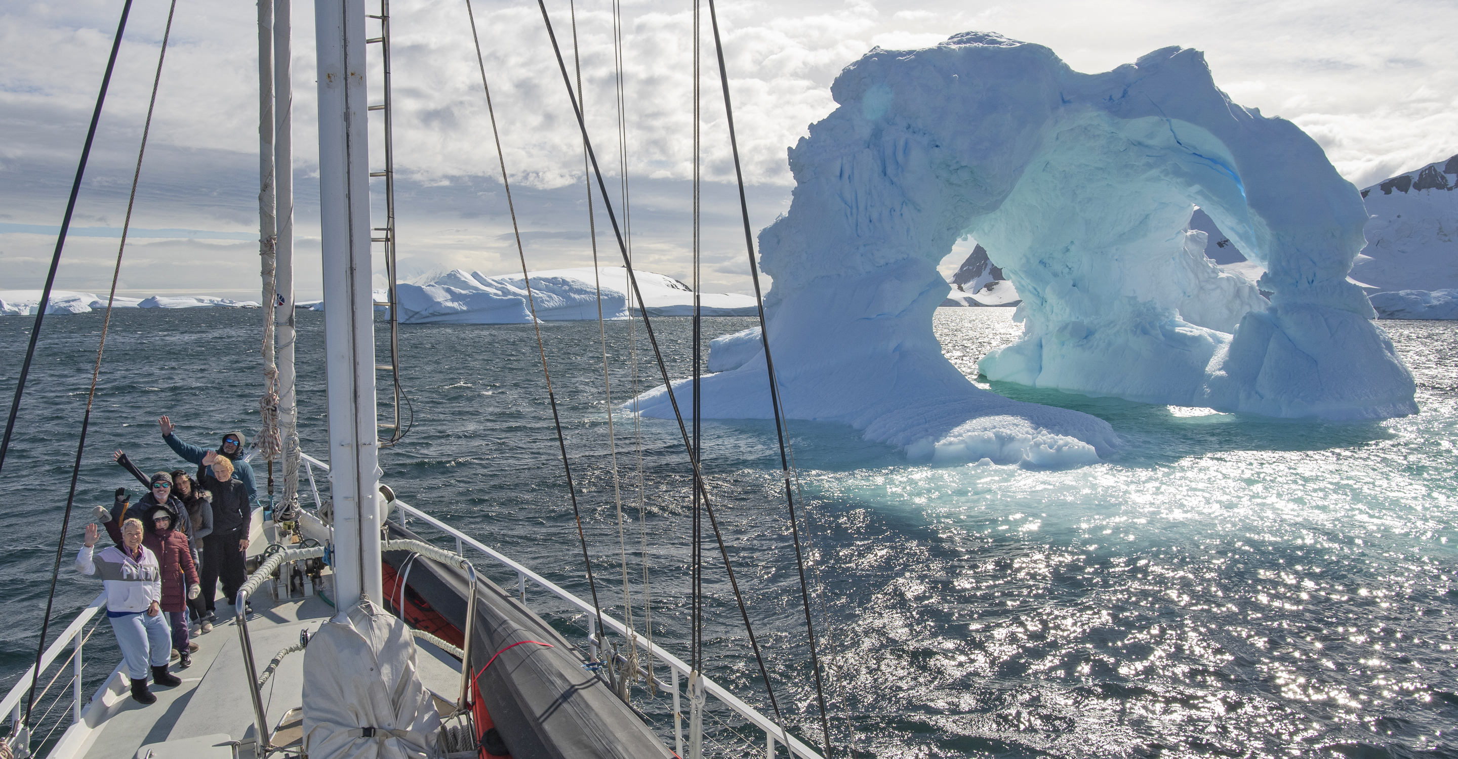 Travelers aboard the S/V Australis wave to the camera as they sail through the waters off Antarctica