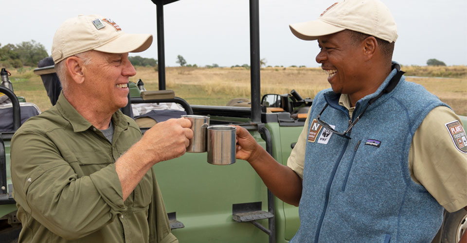A guide and traveler cheers with their coffee cups in Mana Pools National Park, Zimbabwe
