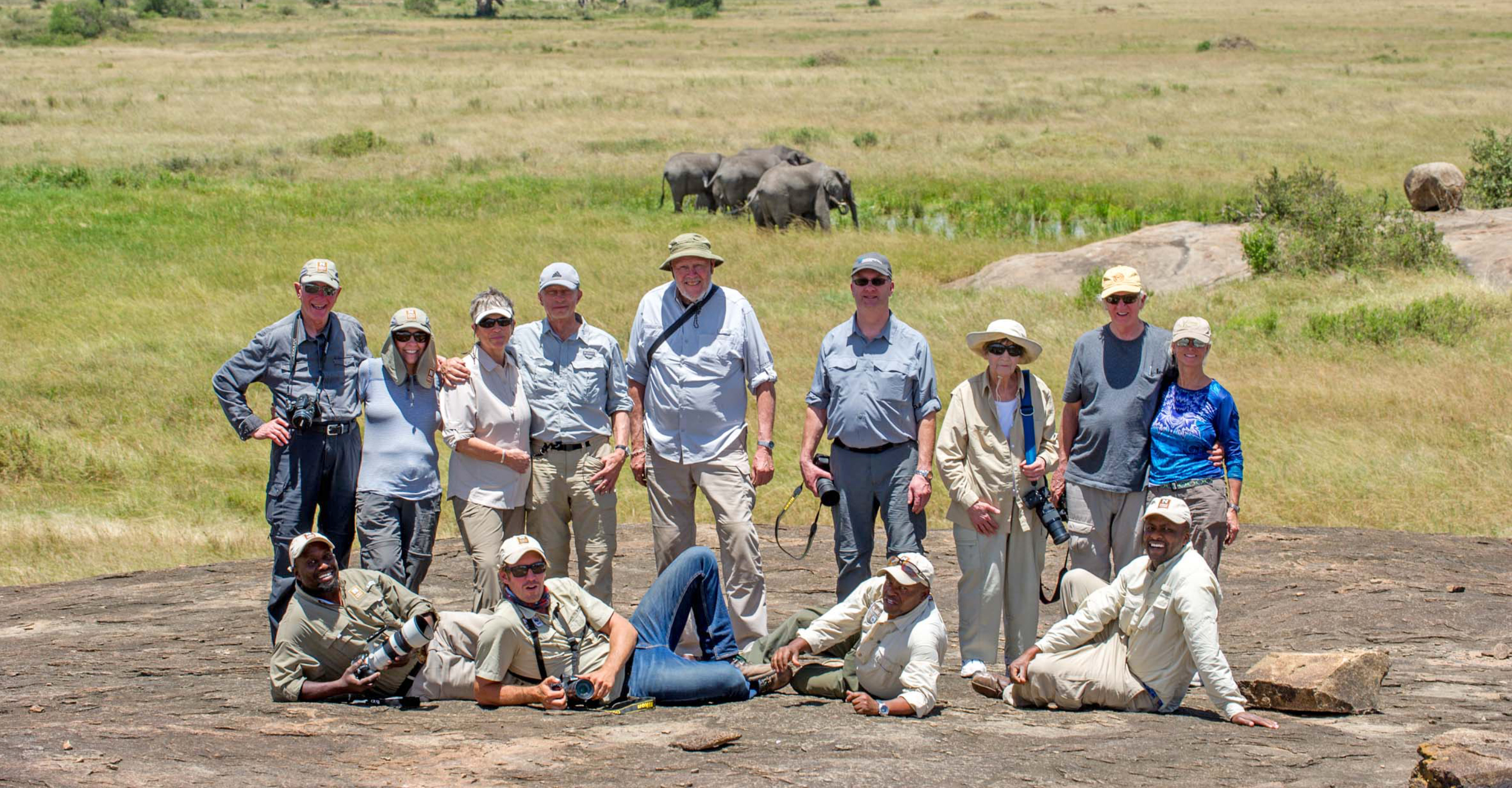 A group of Natural Habitat Adventures travelers and guides pose on a hill near African elephants in the Ngorongoro Crater, Tanzania