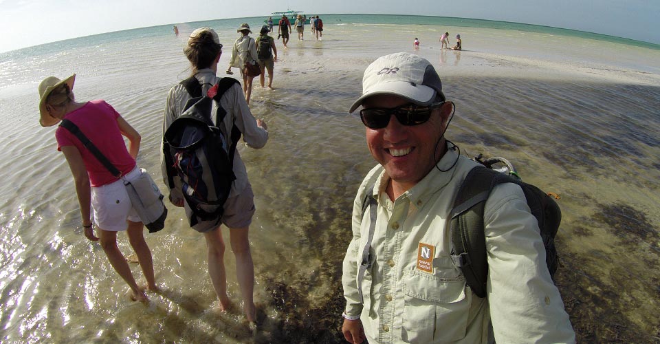 A Natural Habitat Adventures guide smiles on the beach as travelers walk to the snorkeling boat, Isla Holbox, Mexico