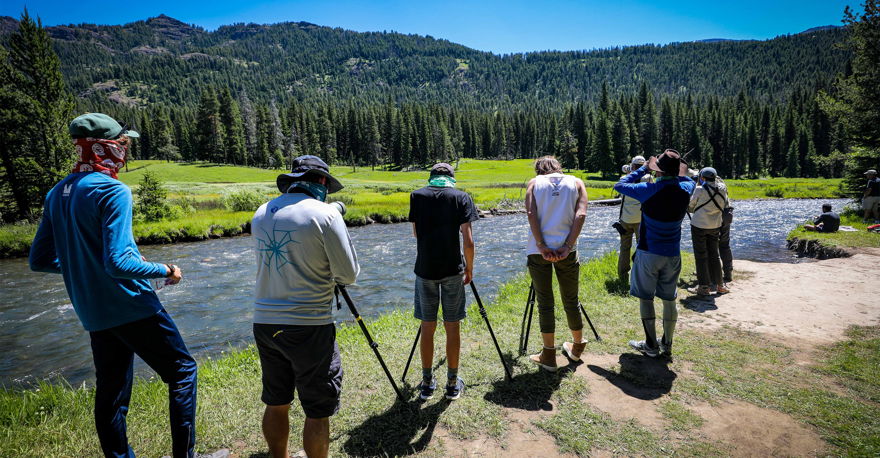 Travelers in Yellowstone National Park stand along the edge of a river and view wildlife through scopes, United States
